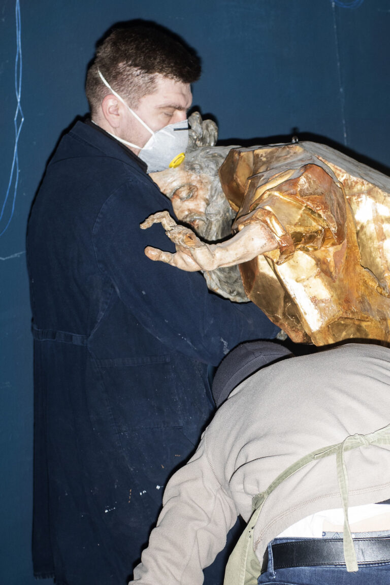 Un altro scatto è stato realizzato durante l'evacuazione delle opere di Pinzel. Il restauratore tiene in mano la figura di Abramo nella scena del sacrificio di Isacco nella chiesa di Ognissanti a Hodowica. La scultura è stata scolpita in legno di tiglio alla fine del 1750. Lviv si trovava al crocevia di influenze settentrionali e meridionali. Essendo collocata alla periferia del mondo cattolico, numerosi architetti di origine italiana furono invitati a lavorare qui, come Paolo Dominici Romanus. Fu anche il luogo in cui alcuni umanisti, come Filippo Buonaccorsi, trovarono rifugio dalle persecuzioni della Chiesa nelle terre italiane. L'influenza settentrionale fu portata in città dai migranti provenienti dai territori tedeschi, soprattutto mercanti e artigiani della Renania e della Sassonia. Anche nell'opera di Pinzel si avvertono gli echi della cultura meridionale e di quella settentrionale: presenta sia l'esuberanza barocca delle sculture religiose in legno di Nicola Fumo, che l’ipertrofia grottesca delle forme delle pale d'altare di Franz Ignaz Günther.